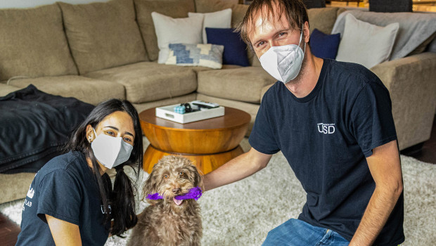 Researchers Amalia Bastos and Patrick Wood pose with one of the canine study subjects in the dog’s home.